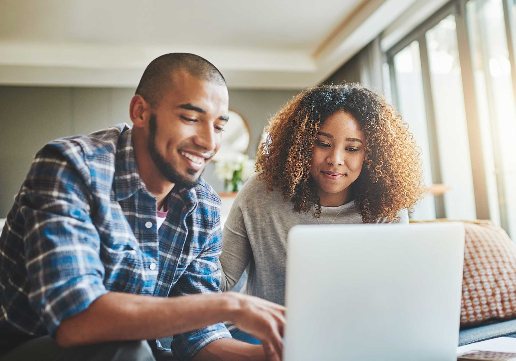 Happy couple sitting in the livingroom looking at their finances on a laptop. 