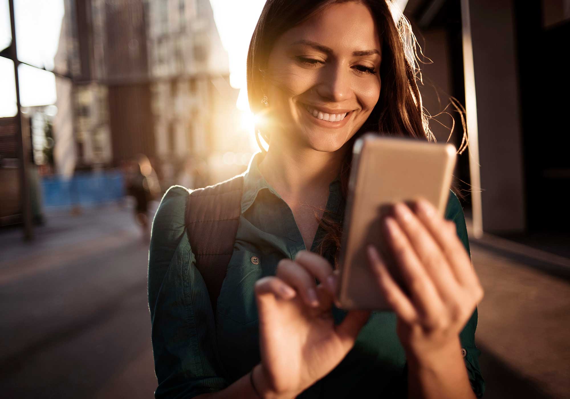 A woman smiling while looking at her iPhone standing on the street. 