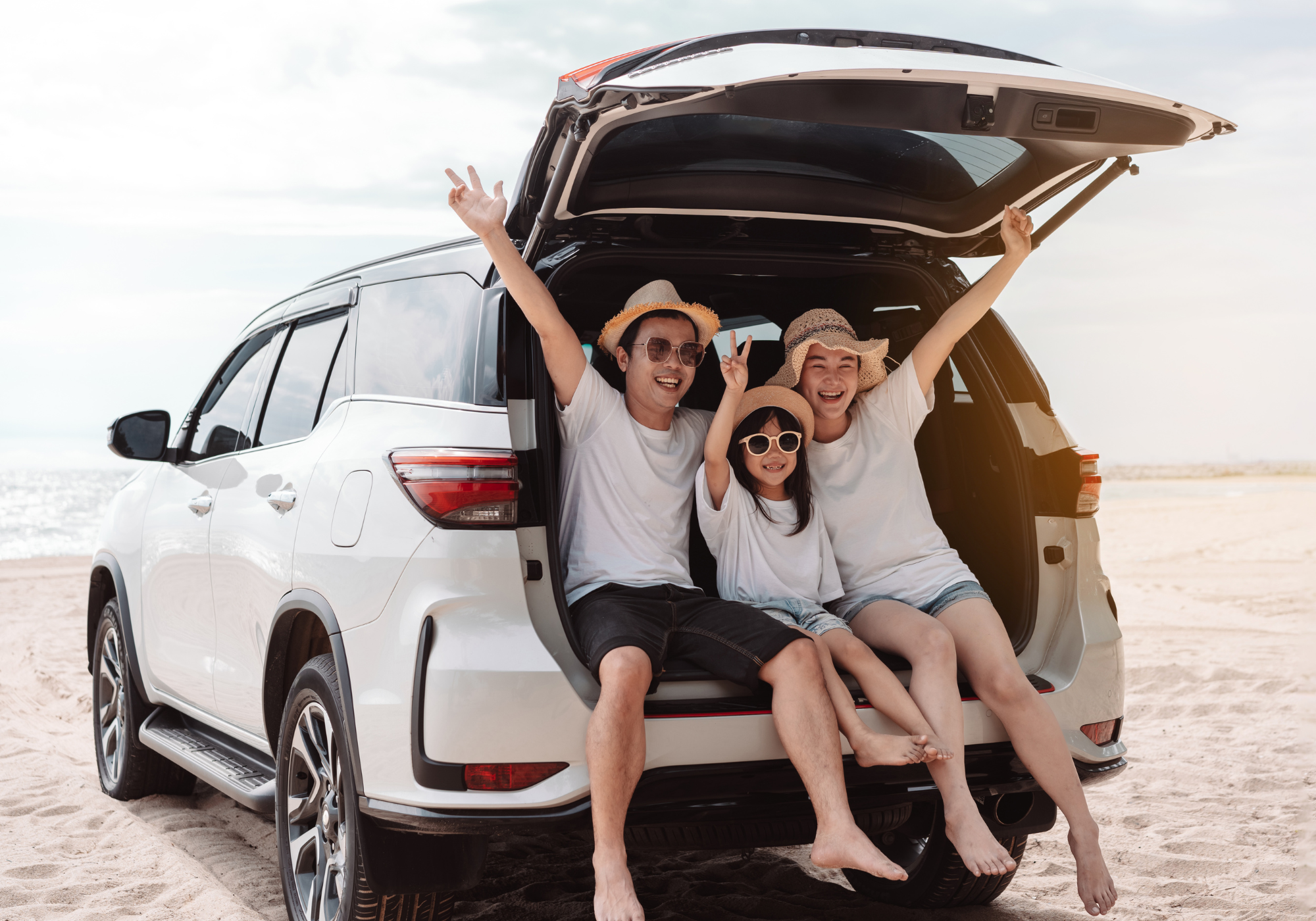 Happy family sitting in the open trunk of an SUV parked at the beach, smiling and enjoying the sunny day together.