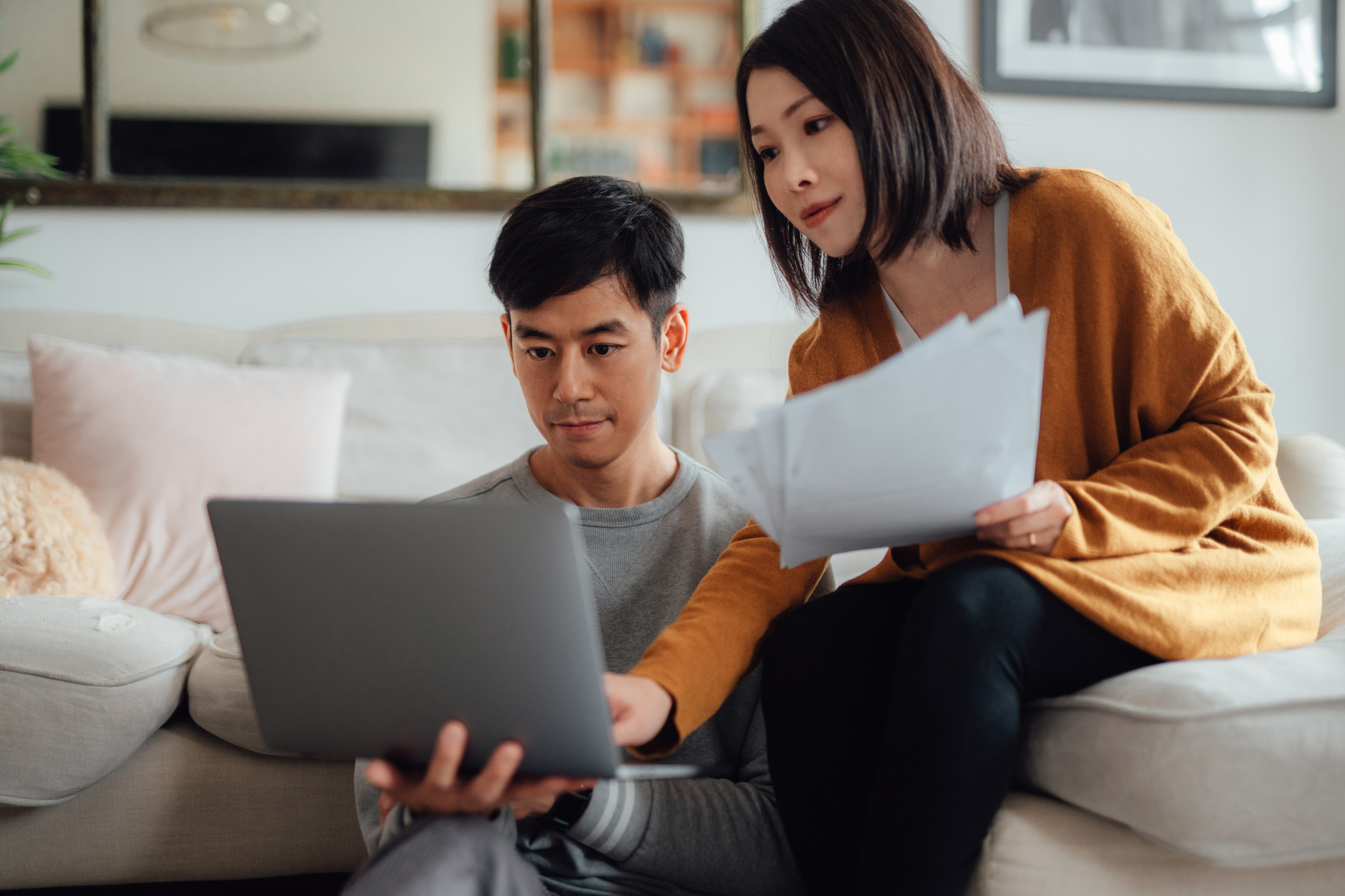 Couple sitting on sofa looking at laptop and paper. 