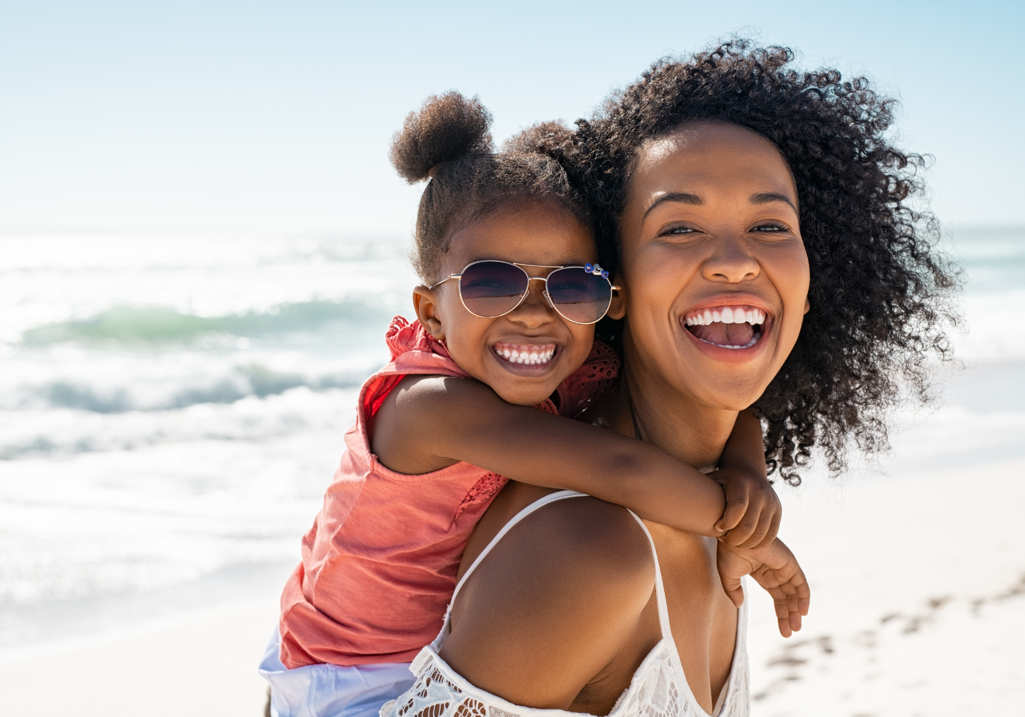 Smiling mother giving her daughter a piggyback ride on the beach.