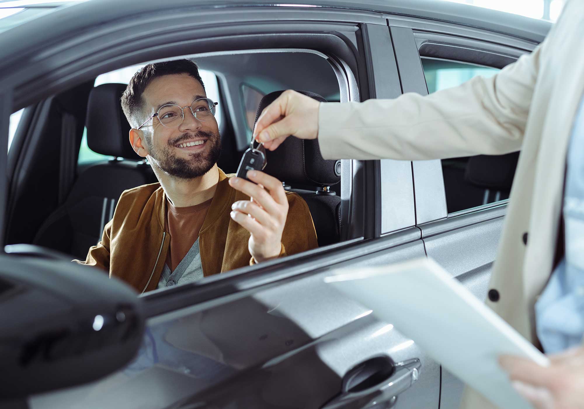 man sitting in new car holding car key