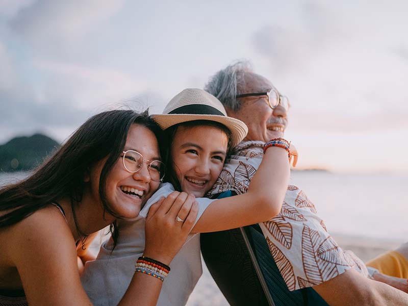 children hugging grandfather at beach