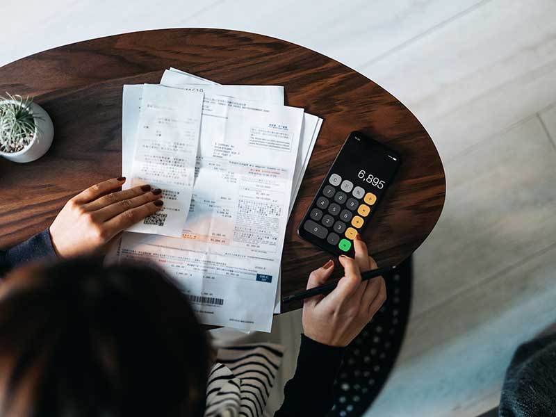 A woman looking at receipts while using her iPhone calculator app.