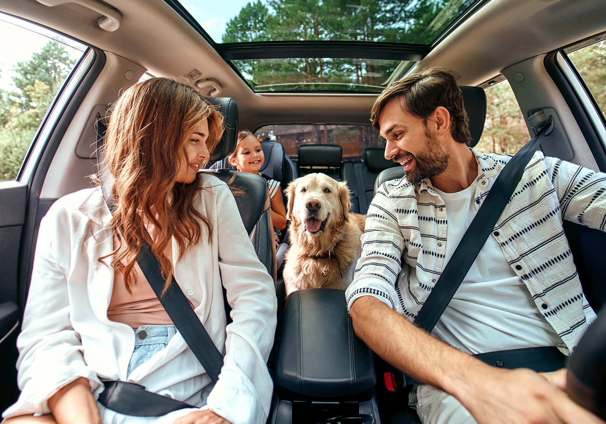 Happy family sitting in SUV with their dog.