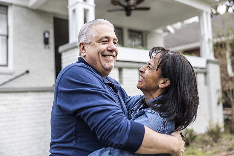 elderly couple hugging standing outside of house