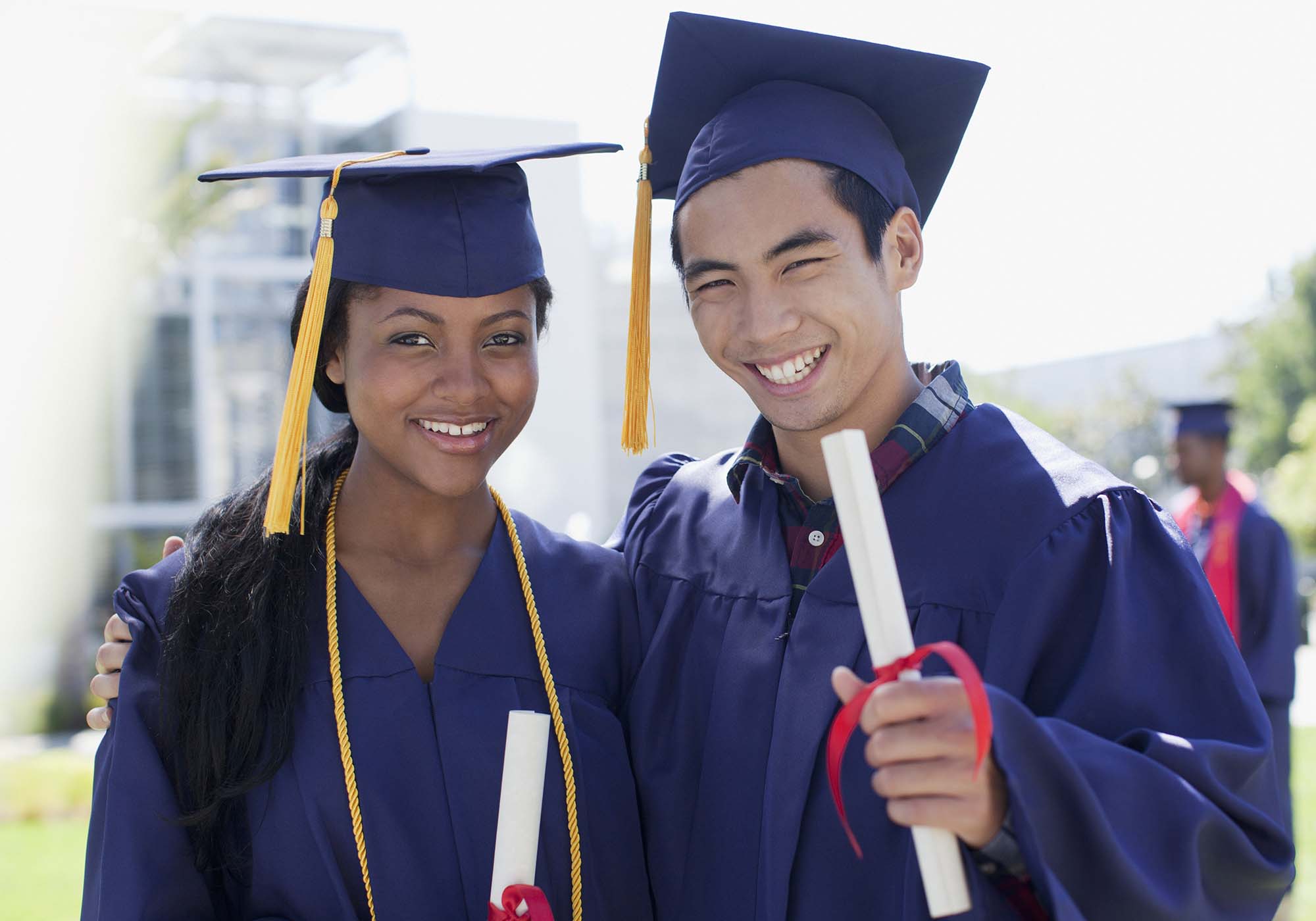 two students at graduation wearing purple cap and gown holding diploma